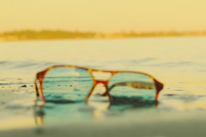 Retro tortoise sunglasses on beach with wave crashing through lenses