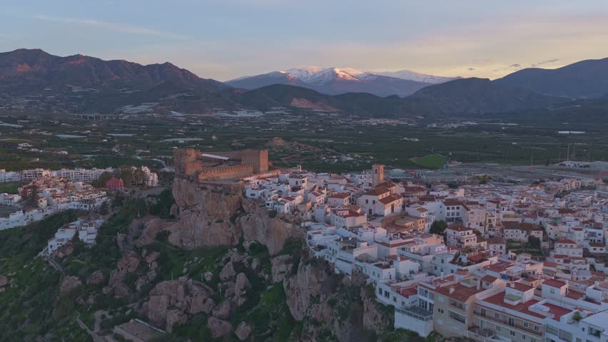 Majestic aerial view of the historic town of salobrena with its medieval castle and the snowy sierra nevada mountains in the background at sunset