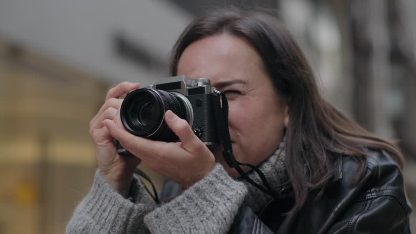 A woman takes photos with a digital camera on a city street. She reviews the picture on the screen and continues shooting.