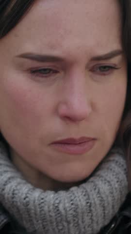 Vertical video of a sad woman crying outdoors. She is upset and wipes away a tear from her eye. Close-up of her face showing grief and despair.