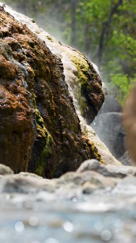 Hot springs with waterfalls in Pai, Thailand, mineral-rich warm water streaming down on volcanic stones under sunlight, natural hot pools used for therapeutic benefits and popular for relaxation.