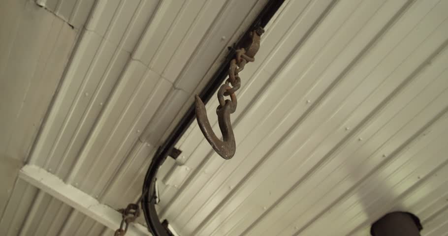 Close-up of a metal hook hanging from a chain inside a farm shed in Brookville, Indiana. Industrial agricultural detail with rustic textures and functional farming equipment.