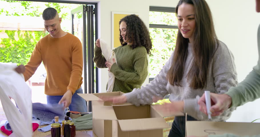 Diverse volunteers sorting and packing donation boxes as they passing basketball at dining table. Community, teamwork, charity, philanthropy, collaborative, greenery, friendly