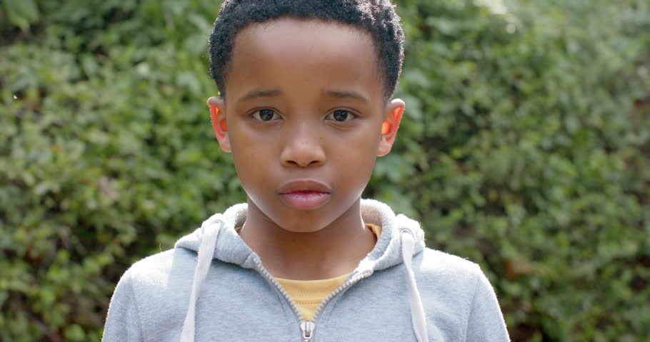 School-age boy speaking, flexing, and smiling proudly in backyard wearing hoodie and yellow T-shirt. Youth, confidence, strength, outdoor, positivity, casual, energetic