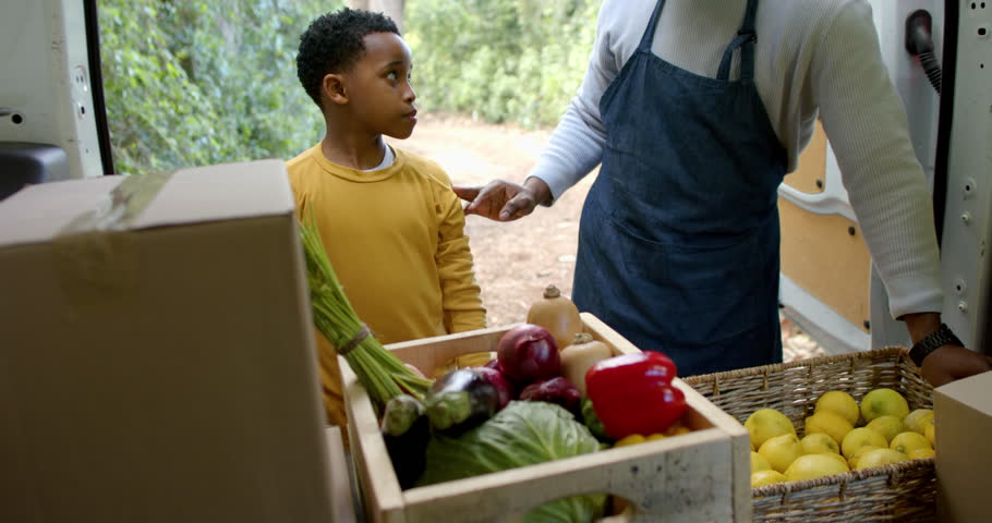 African American father and son by van exchanging high fives bumping fists while learning produce. Family, mentorship, freshness, agriculture, community, outdoor, positivity