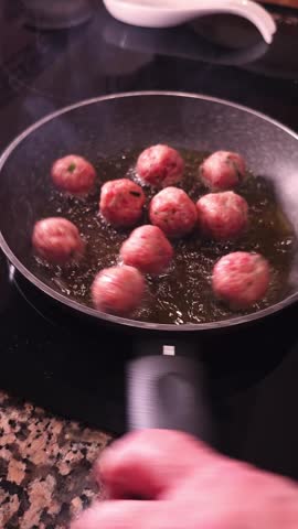 Meatballs frying in olive oil pan on stovetop with steam and sizzling motion. Mediterranean and Spanish cuisine.