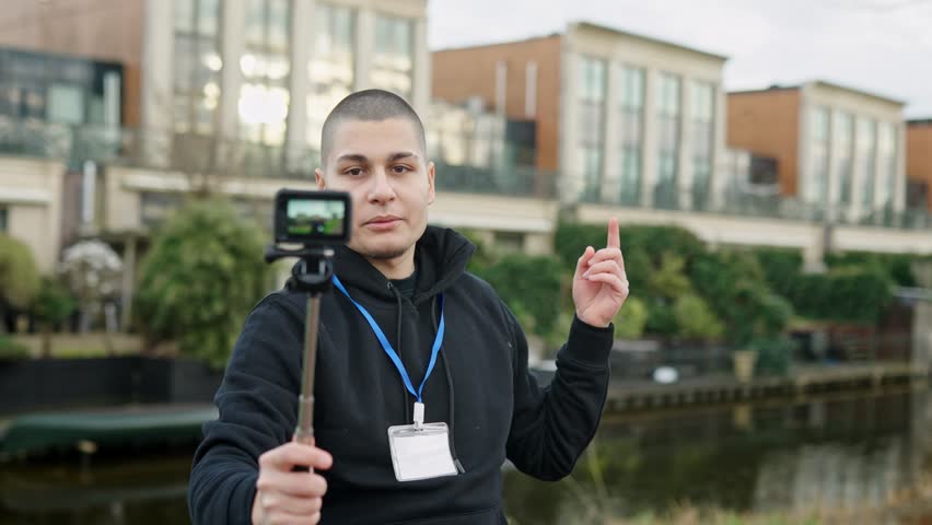 Enthusiastic male journalist or vlogger with a press pass recording a video blog with an action camera for his social media channel