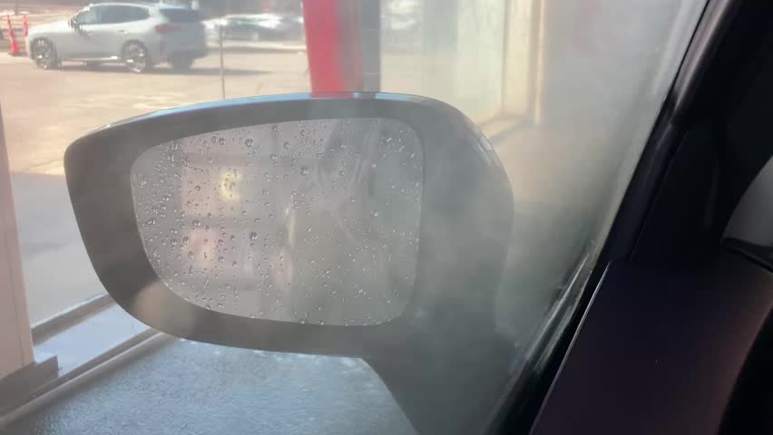 Horizontal selective focus view of side mirror seen through window covered in suds during car wash