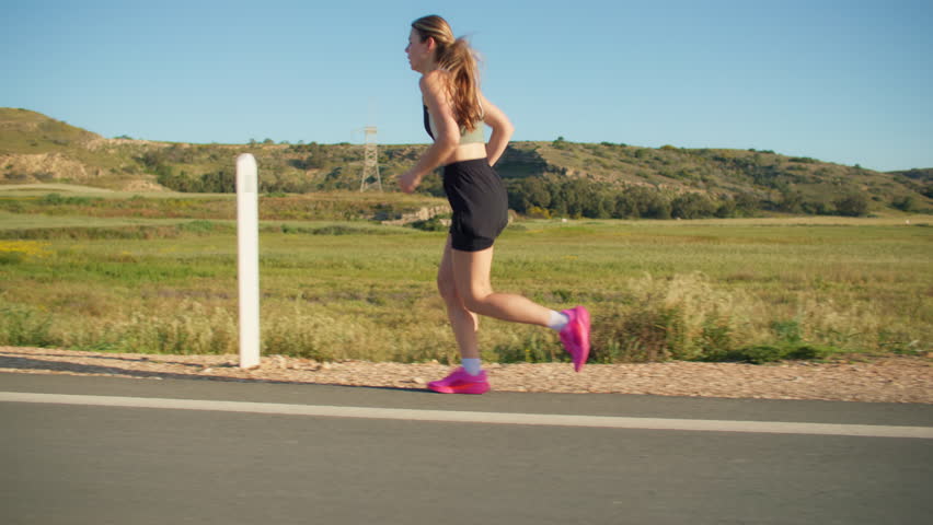 Athletic sporty woman jogging along country road in morning light surrounded by nature with fitness training and healthy lifestyle