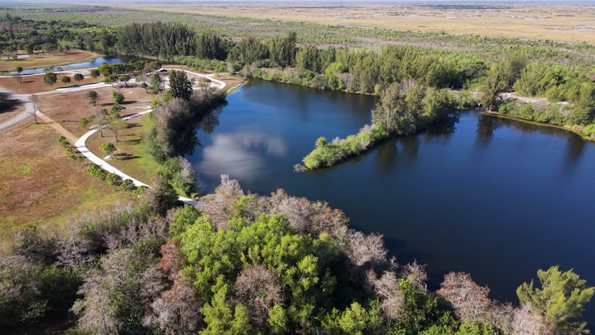 Aerial orbit of a pond at West Delray Regional Park in Delray Beach Florida on a sunny clear day showing a large island in the pond and green lush surrounding area.