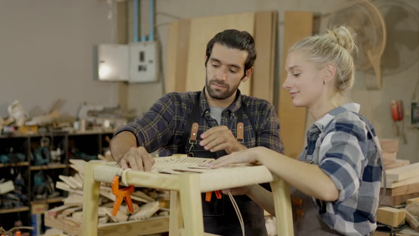 Carpenter woodworking workshop furniture table teamwork wood craftsman craftswoman tool two carpenters and apprentice sanding measuring clamping wooden table and stool studio, focused guidance