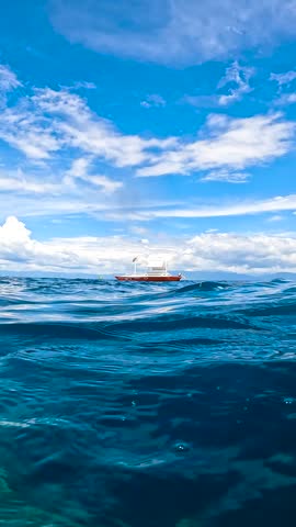 Traditional outrigger boat floating on the blue ocean surface under a cloudy sky in Moalboal, Cebu, Philippines.