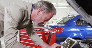 Senior tech placing laptop on fender starting auto scan, leaning, typing while HUD showing data. Diagnostics, mechanic, workshop, engine, computer, overlay, automotive - Powered by Shutterstock - Get 15% off with code: PIKWIZARD15