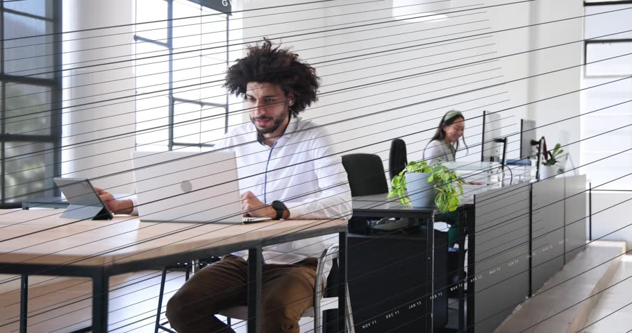 Man typing laptop in office as camera shifts, woman answering phone, frosted glass creating privacy. Openplan, coworking, partition, sunlit, screens, tablet, diagonal