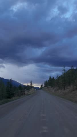 Heavy Haul Truck Drives on Remote Dirt Road Through British Columbia Mountains Under Dramatic Sky