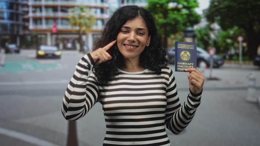 Young woman holding belarus passport and pointing finger to temple on a city street; identity confidence travel.