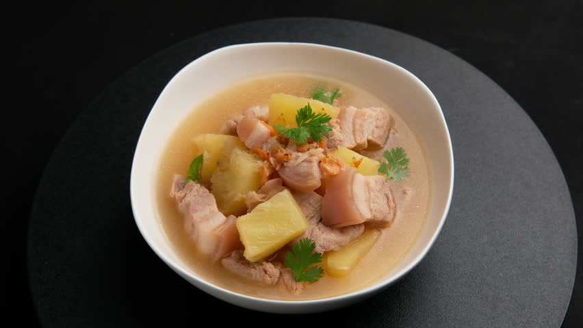 Thai soup with tender pork belly and sweet pineapples in white bowl.