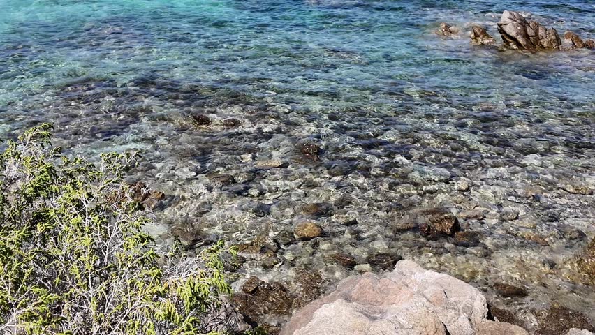 Transparent water with visible rocks and ripples. Calm seaside background with natural details. Italy Sardinian Rena Bianca 