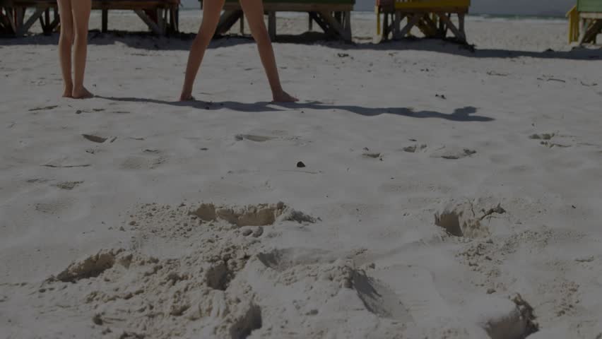Vertical video: Two girls coming holding hands, trying balance by huts while blue overlay forming. Beach, equilibrium, friendship, pair, barefoot, sunny, constellation