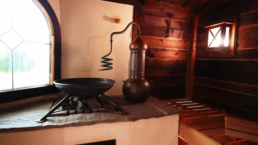 Warm interior shows copper alembic, sauna stones, arched leaded window, and wood walls in an Ischgl hotel spa, Austria, as the camera pans to the spiral condenser.