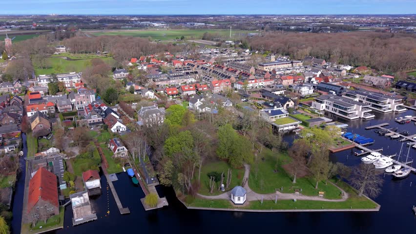 Aerial drone view of a wealthy Dutch waterfront neighborhood with luxury villas, a marina, and lush parks. Modern residential architecture and green living in the Netherlands from a high angle.