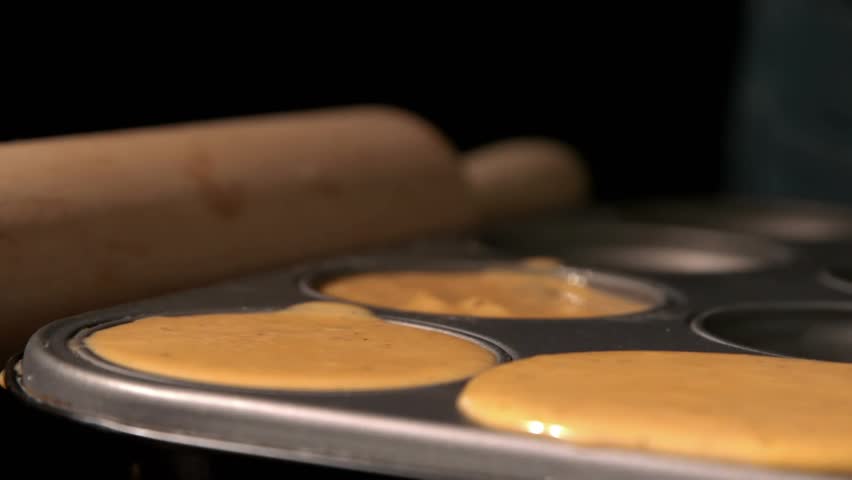 Hand approaching and placing chocolate into batter for baking, confetti drifting, chocolate sinking. Muffin, tray, cocoa, goldflakes, glitter, kitchen, closeup