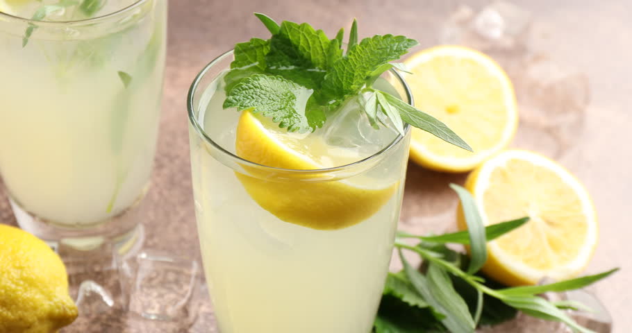 Putting tarragon leaves onto tasty lemonade in glass on grey table, closeup