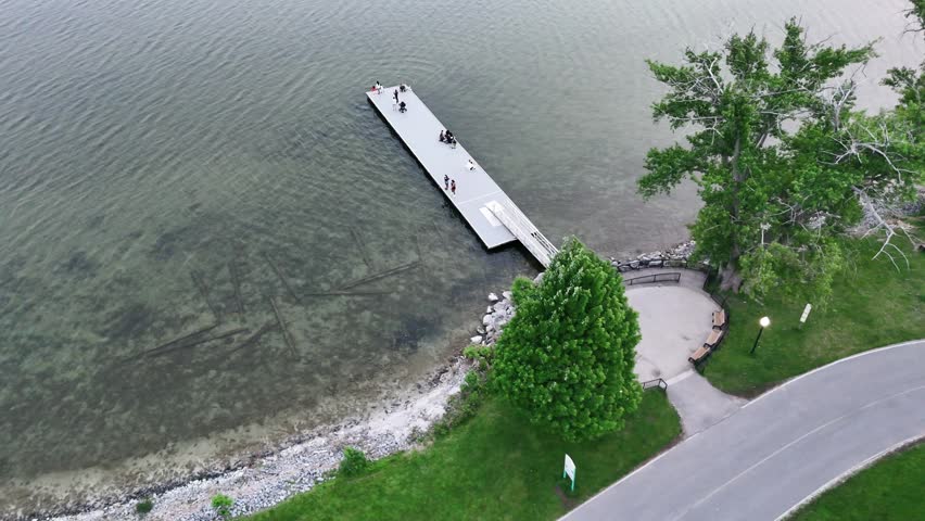 People enjoying the calm waters and fishing from a dock that extends out into the lake within a public park.