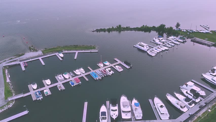 Boats and other nautical vessels docked at a small harbor while the sun sets and imposes a relaxing tone across the surrounding surface of the water in this lake.