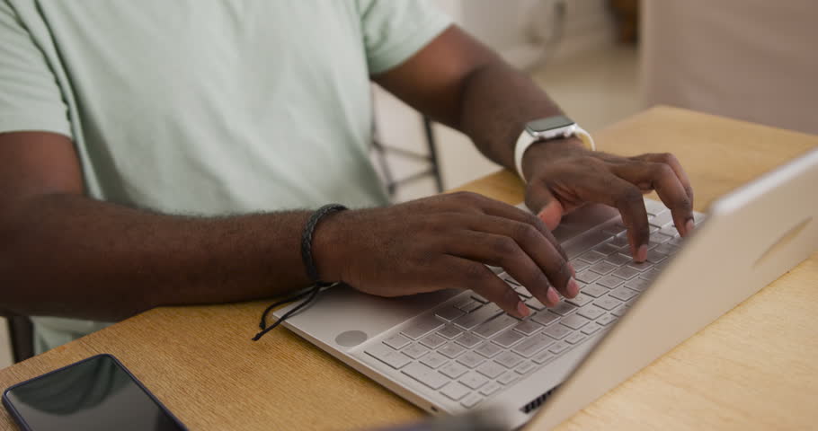 Mid adult African man placing hands on laptop keyboard, typing and working at wooden table. Remote, freelancer, homeoffice, productivity, concentration, calm, modern