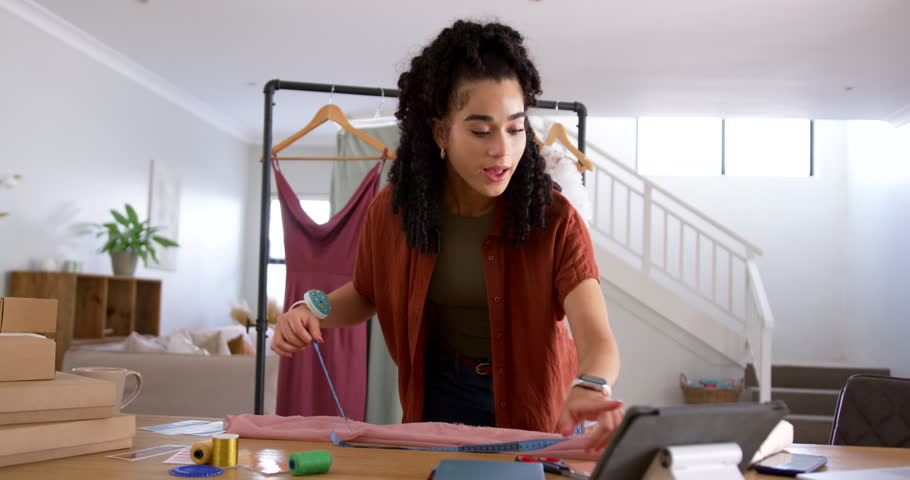 Adult woman checking tablet, measuring pink fabric with tape, marking and cutting for garment. Seamstress, dressmaking, textiles, pattern, cut, sewing, homestudio