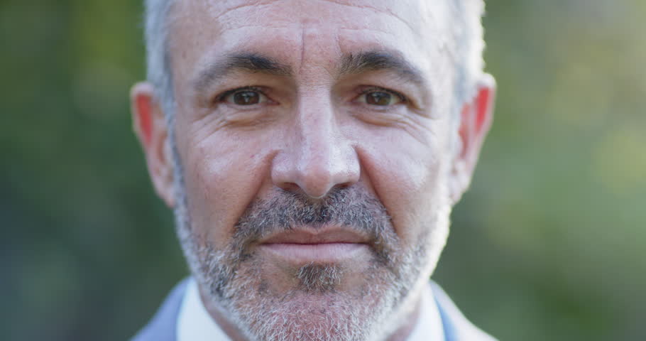 Middle-aged man responding to off-camera cue, smiling while facing camera outdoors in suit. Closeup, portrait, headshot, male, adult, blazer, nature