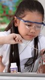 Young Asian girls wearing safety goggles pour red liquid into a volcano model during class - Powered by Shutterstock - Get 15% off with code: PIKWIZARD15