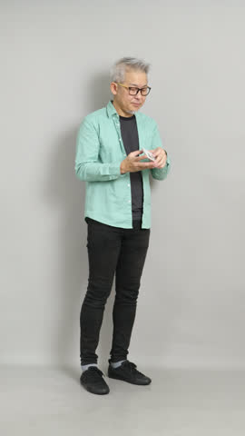 Mature Asian man holding his phone as a camera, crouching slightly and talking happily while taking a picture.