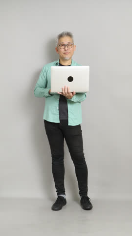 Front view of a successful mature entrepreneur looking at the camera with a big smile and giving a thumb up while holding his laptop.