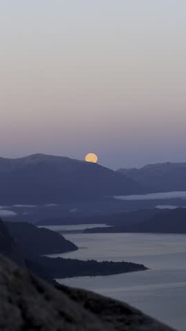Full Moon Rising Over Mountain Peaks and Calm Lake at Twilight Blue Hour