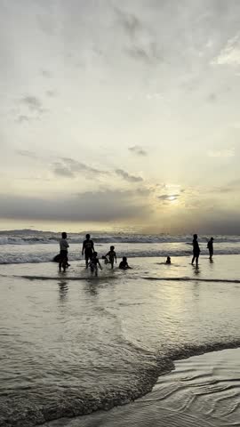 Silhouette footage of people playing on the beach during sunset with reflection on wet sand, creating emotional and cinematic coastal scene.