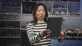 Young chinese woman holding a tablet and pointing a finger at its screen while furrowing her brow at a bakery counter; confusion. - Powered by Shutterstock - Get 15% off with code: PIKWIZARD15