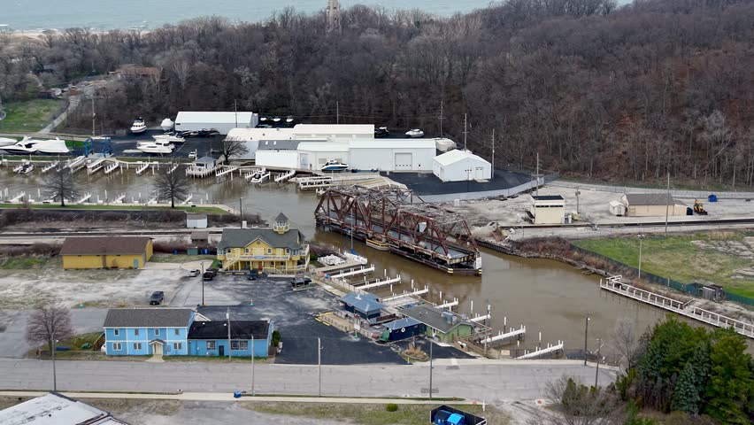 Industrial railroad swing bridge turning to allow boat traffic through a small town marina