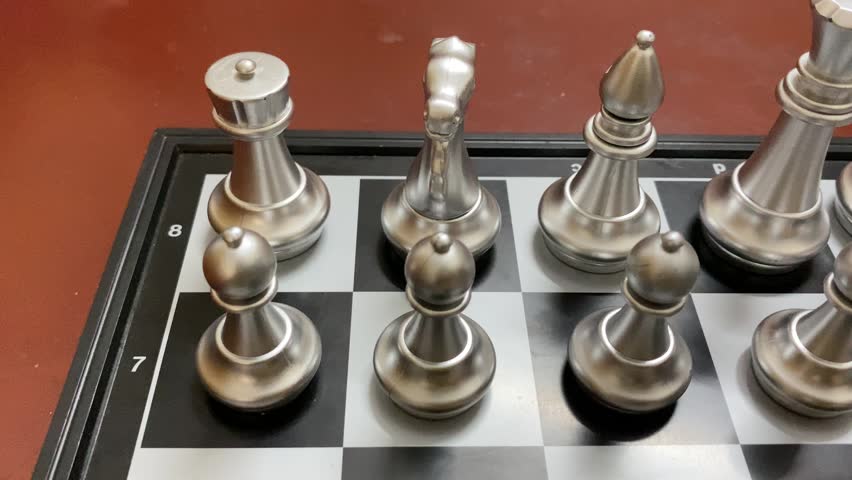 Indoor game: Silver colored chess pieces arranged on a board, ready to start game.