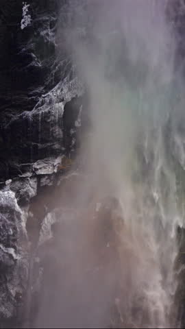 Vertical Screen: Yosemite National Park winter waterfall plunges down dramatic rocky cliff creating dense mist and spray against dark wet rock formations in natural wilderness