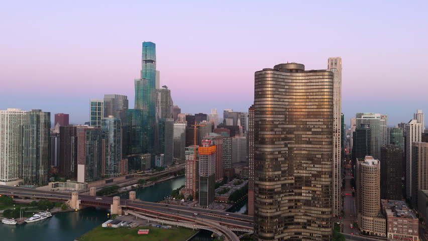 Aerial drone footage captures stunning Chicago skyline at dusk with golden light reflecting off glass skyscrapers, purple and pink hues painting sky as camera pans across bustling downtown riverfront.