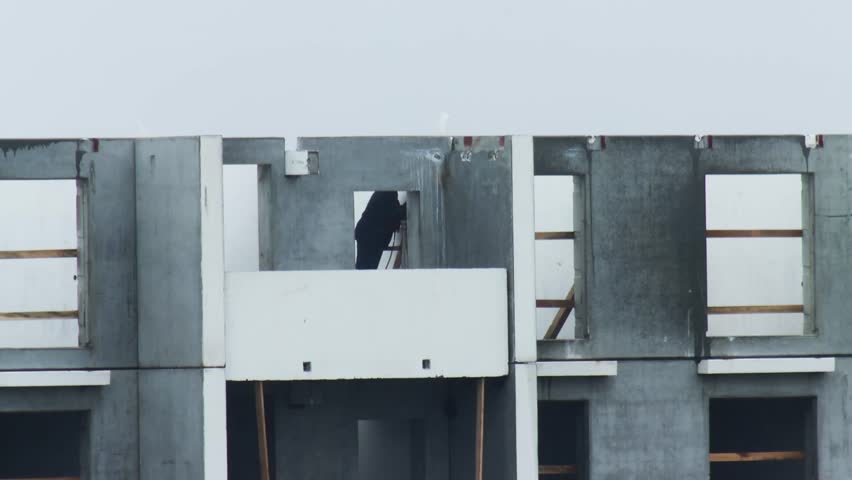 Construction worker on ladder inside unfinished multi-story residential building. Structure of grey prefabricated concrete wall slabs. Building development project, exposed framework.