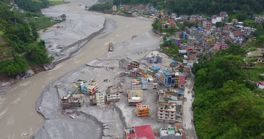 Drone shot of houses buried in silt near the Melamchi River after flooding, surrounded by forest and damaged landscape in Sindhupalchowk Nepal.