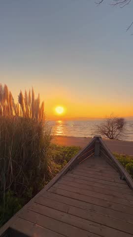 A stunning vertical view of the low-hanging red sun casting a shimmering path across the lake towards a traditional wooden boat.