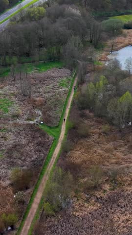 Panshanger Park vertical aerial pan over lakeside wetlands and the A414 highway, showing woodland edges and open parkland in fresh spring colours, Hertfordshire, England.