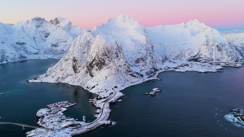 Breathtaking aerial view of snowcovered peaks and traditional fishing villages in Lofoten, Norway during a pink winter sunset.