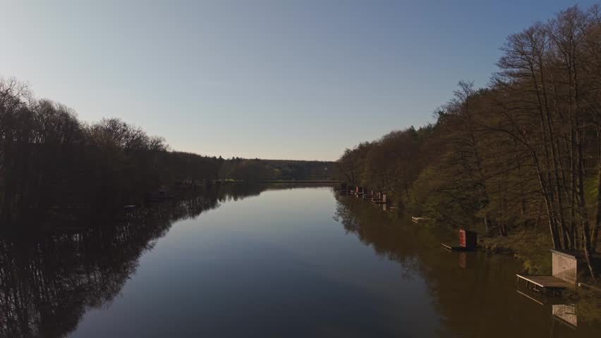 Drone flying over a calm fishing lake surrounded by dense forest on both sides.