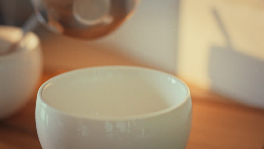 A skilled barista carefully pours a rich, hot beverage into a delicate white cup from a traditional Turkish coffee cup. The process showcases the art of crafting Turkish coffee, a beloved drink