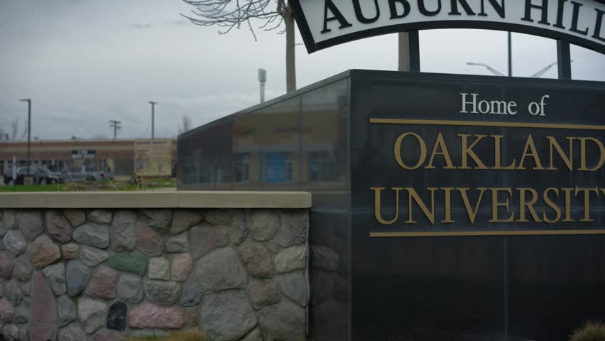 Pan right shot of the Oakland University sign in Auburn Hills Michigan at a campus entrance in daylight with smooth cinematic motion